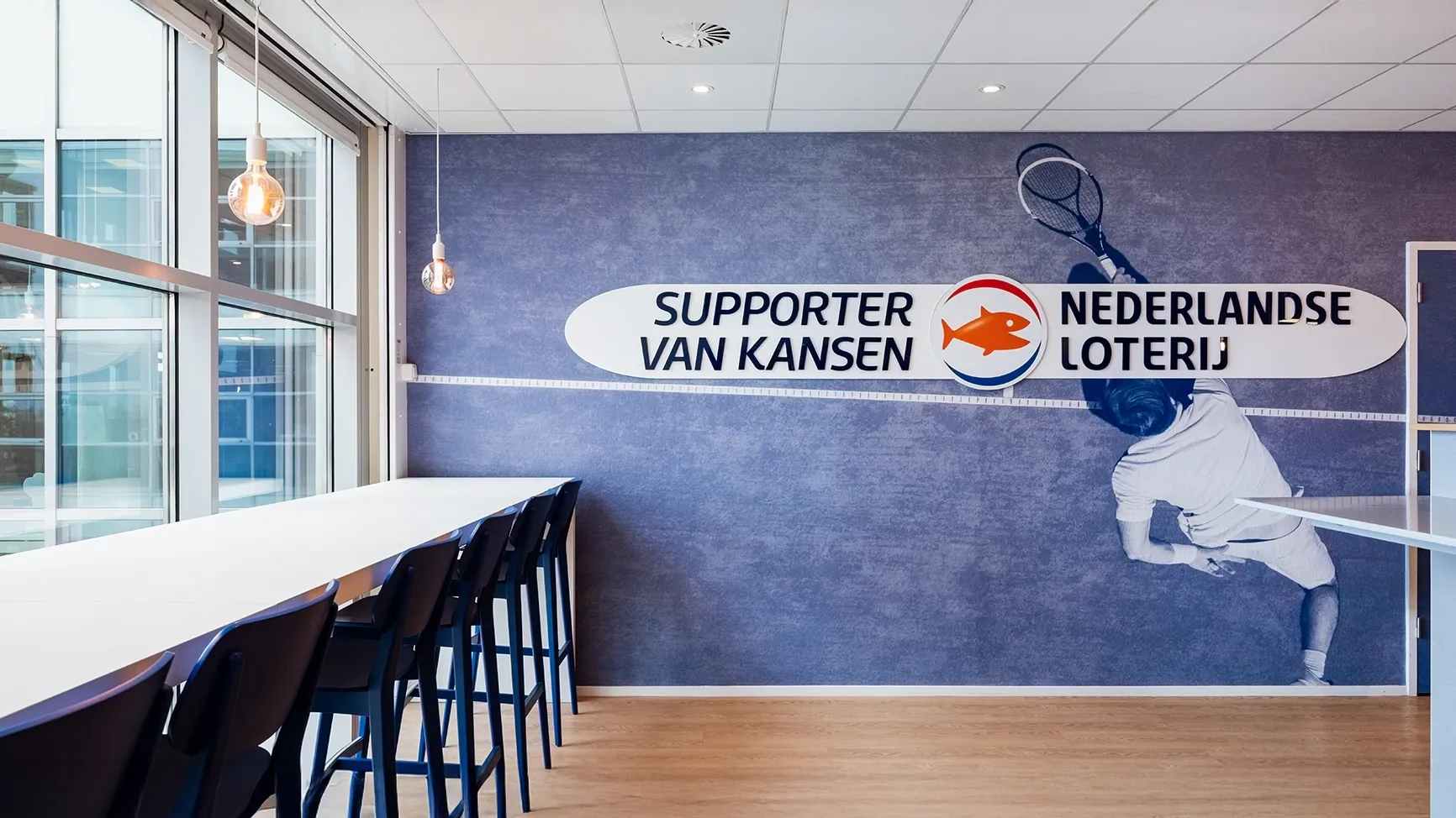 Een moderne ruimte met hoge tafels, een blauwe wand met een tekst en een afbeelding van een tennisser.
