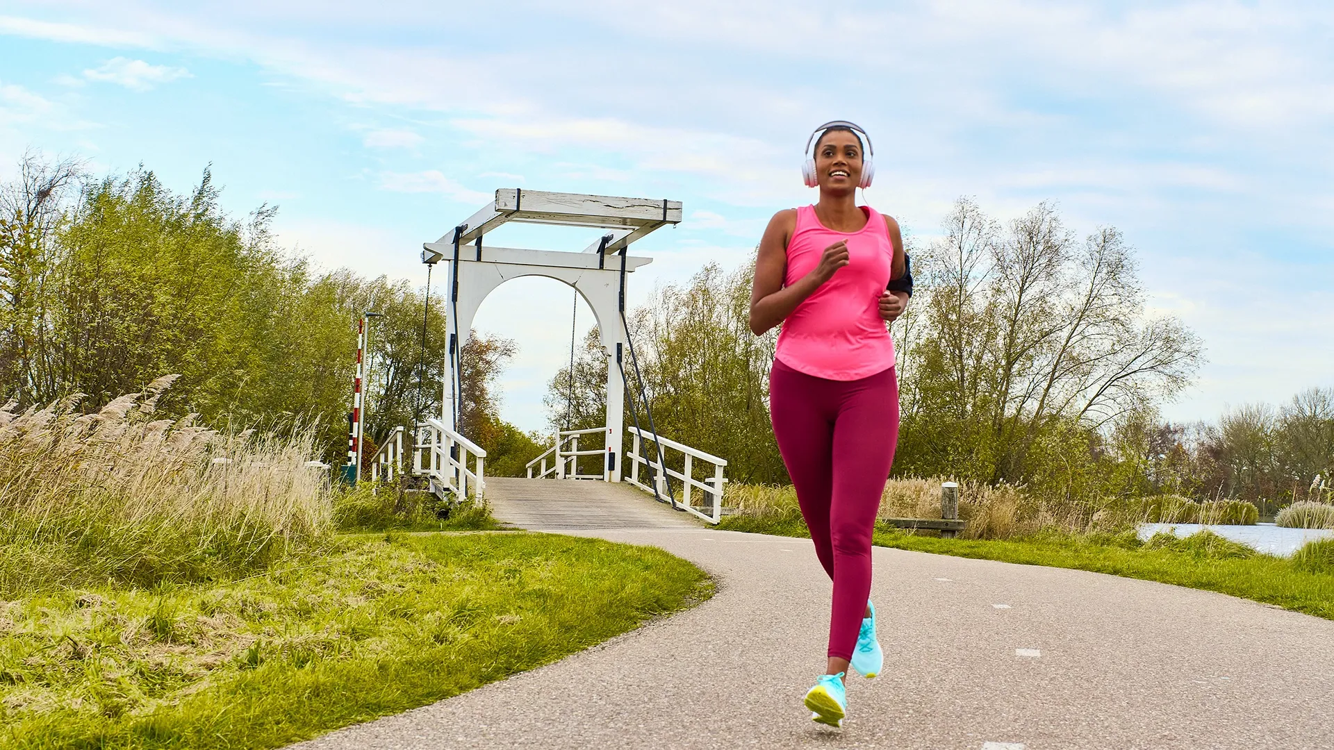 Een persoon in sportkleding jogt langs een brug in een groene omgeving.
